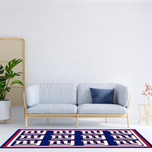 May include: A blue and white rug with the letters "NY" repeated in a pattern. The rug is in front of a light blue sofa with a blue pillow. There is a plant in a white pot and a small table with a vase of flowers on it.