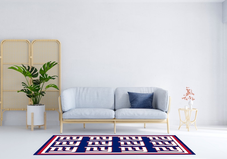 May include: A blue and white rug with the letters "NY" repeated in a pattern. The rug is in front of a light blue sofa with a blue pillow. There is a plant in a white pot and a small table with a vase of flowers on it.