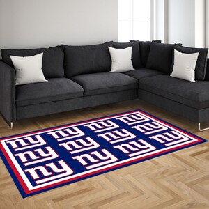 May include: A blue and red rug with the letters "NY" repeated in white. The rug is on a hardwood floor in front of a gray sectional sofa.