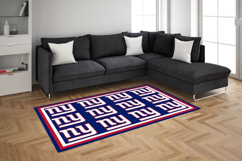 May include: A blue and red rug with the letters "NY" repeated in white. The rug is on a hardwood floor in front of a gray sectional sofa.
