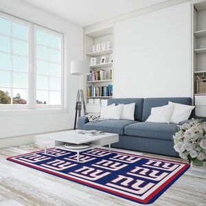 May include: A blue and white area rug with the New York Giants logo repeated in a pattern. The rug is on a white wood floor in a living room with a blue couch and a white coffee table.