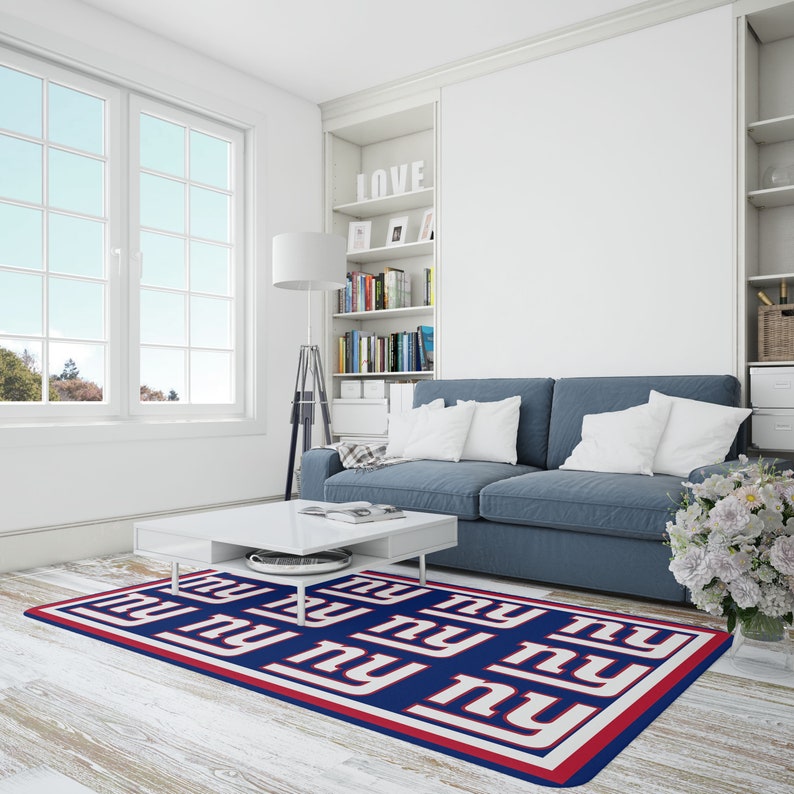 May include: A blue and white area rug with the New York Giants logo repeated in a pattern. The rug is on a white wood floor in a living room with a blue couch and a white coffee table.