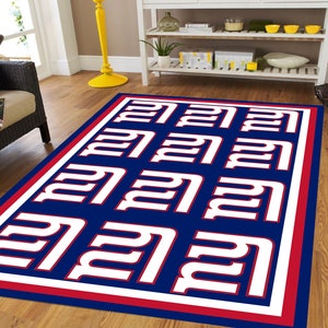 May include: A blue and red rug with a white repeated pattern of the New York Giants logo. The rug has a red and white border.