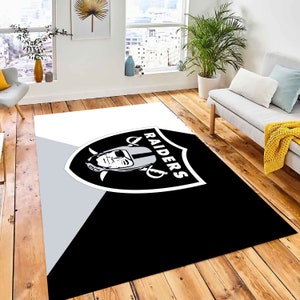May include: Black and white area rug with the Las Vegas Raiders logo. The logo features a shield with a football player's helmet and the word "RAIDERS" written vertically.