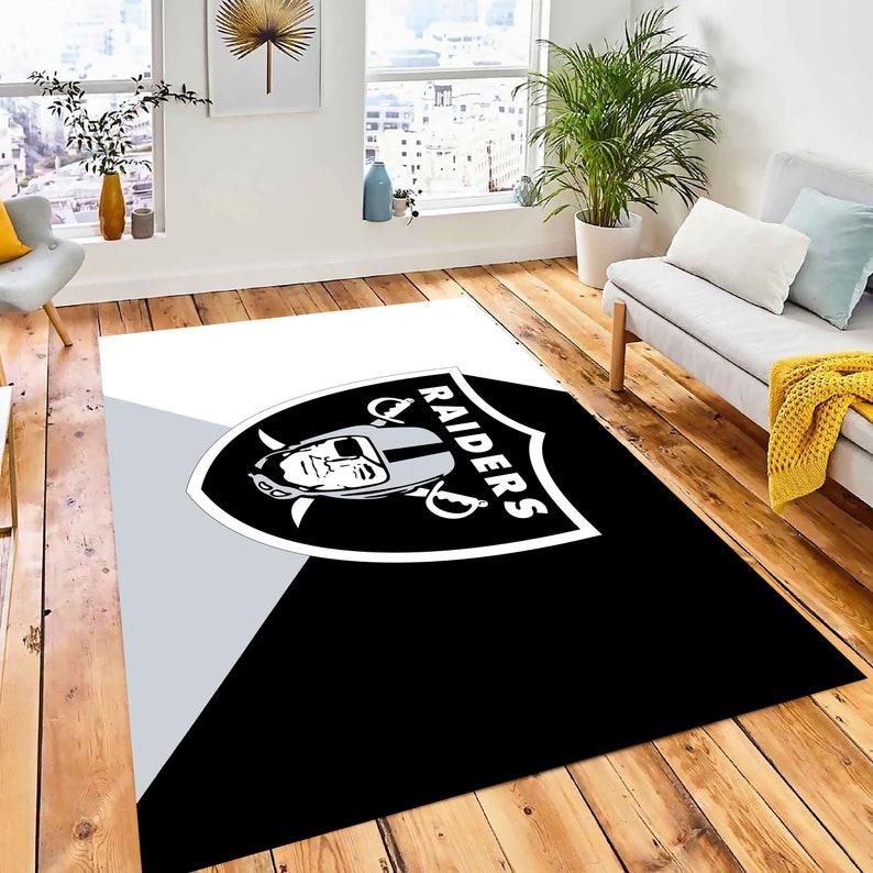 May include: Black and white area rug with the Las Vegas Raiders logo. The logo features a shield with a football player's helmet and the word "RAIDERS" written vertically.