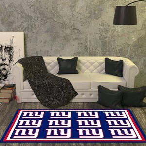 May include: A blue and red rug with the letters "NY" repeated in a grid pattern. The rug is in a living room setting with a white couch and black pillows.