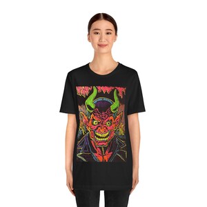 May include: Black t-shirt with a neon green, pink, and red graphic print of a devil with horns. The devil is wearing a black leather jacket.