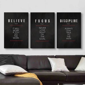 May include: Three motivational wall art prints with black backgrounds. The prints feature the words "BELIEVE", "FOCUS", and "DISCIPLINE" in silver text, each with a definition and a motivational quote. The prints are displayed above a black leather couch.
