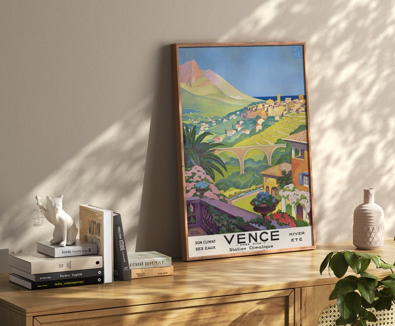 K&ouml;nnte beinhalten: Ein Vintage-Reiseposter f&uuml;r die Stadt "Vence" in Frankreich. Das Poster zeigt eine farbenfrohe Illustration einer Stadt am Hang mit einer Br&uuml;cke, Palmen und Blick auf das Mittelmeer. Der Text auf dem Poster lautet "Vence Station Climatique Son Climat Ses Eaux Hiver Ete".