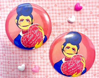 Può includere: Due spille rotonde rosa con un personaggio dei cartoni animati con i capelli blu che tiene in mano un biglietto a forma di cuore con la scritta "I Love You". Lo sfondo è un motivo a scacchi rosa e bianco con decorazioni a forma di cuore.