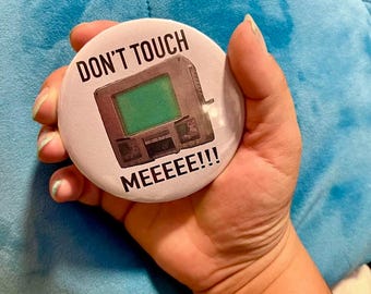 May include: A white button with a retro computer graphic and the text "DON'T TOUCH MEEEEEEE!!!"