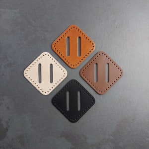 May include: Four diamond-shaped leather patches with two parallel slits cut out. The patches are in beige, brown, black, and orange.