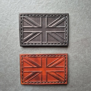 Peut inclure: Deux patchs en cuir avec le motif du drapeau de l'Union Jack. Le patch du haut est en cuir noir et le patch du bas est en cuir marron.