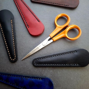 May include: A set of five leather sheaths in black, blue and red, with a pair of yellow-handled scissors with a silver blade. The scissors are labelled "Fiskars 100" Made in Finland.