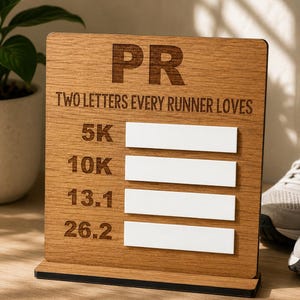 May include: Wooden sign with the letters "PR" and the text "TWO LETTERS EVERY RUNNER LOVES." The sign has slots for 5K, 10K, 13.1, and 26.2 distances. The sign is made of light brown wood.