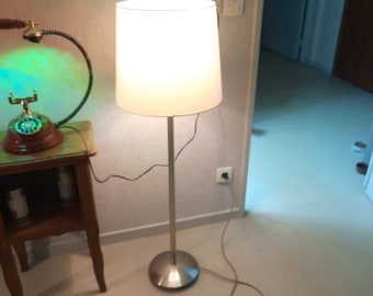 Silver metal floor lamp with large white lampshade.
