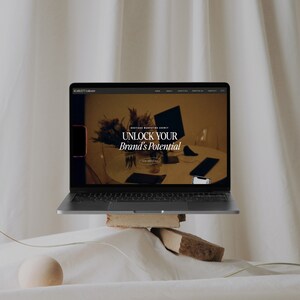 May include: A laptop computer displaying a website for Scarlett Collective, a boutique marketing agency. The website features the text "Unlock Your Brand's Potential".