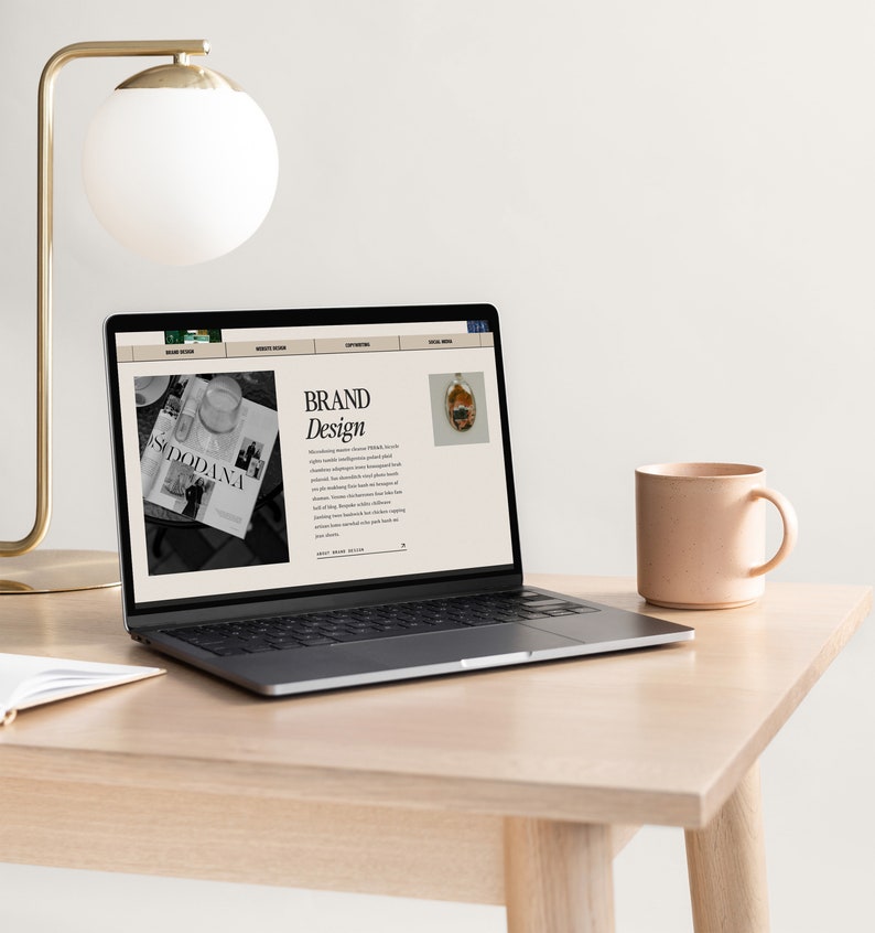 May include: A laptop computer with a website open on the screen. The website is about brand design and features a black and white photo of a magazine and a photo of a small, colorful object. The laptop is on a light wood desk with a white mug and a lamp.