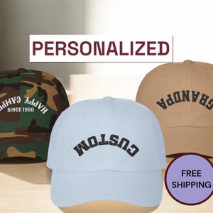 K&ouml;nnte beinhalten: Drei Baseballkappen mit verschiedenen Designs. Die erste Kappe ist Tarnmuster mit dem Text "Happy Camper Since 1980". Die zweite Kappe ist hellblau mit dem Text "Custom" in Schwarz. Die dritte Kappe ist beige mit dem Text "Grandpa" in Schwarz.