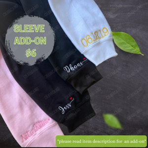 May include: Close-up of personalized sweatshirt sleeves in black, white, and pink. The sleeves are embroidered with names and dates in various colors. The text "SLEEVE ADD-ON" is visible in a green circle.