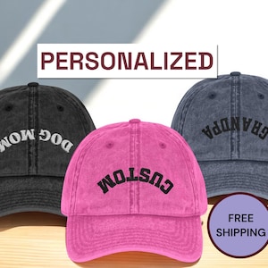 May include: Three personalized baseball caps in black, pink, and blue. The black cap says "DOG MOM", the pink cap says "CUSTOM", and the blue cap says "GRANDPA". The word "PERSONALIZED" is above the caps.