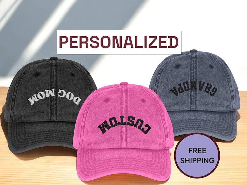 May include: Three personalized baseball caps in black, pink, and blue. The black cap says "DOG MOM", the pink cap says "CUSTOM", and the blue cap says "GRANDPA". The word "PERSONALIZED" is above the caps.