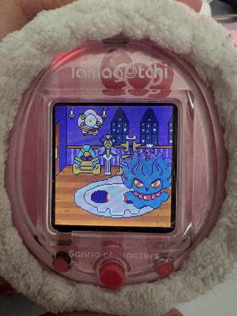 Puede incluir: Una mascota digital Tamagotchi rosa con una funda blanca y esponjosa. La pantalla muestra una escena pixelada con un personaje azul con forma de fantasma. El texto "Sanrio characters" es visible en el dispositivo.