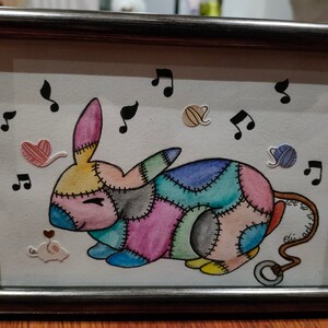 Peut inclure: Une peinture à l'aquarelle encadrée d'un lapin en patchwork avec un nez rose et une queue avec un anneau. Le lapin est entouré de notes de musique et de pelotes de laine.
