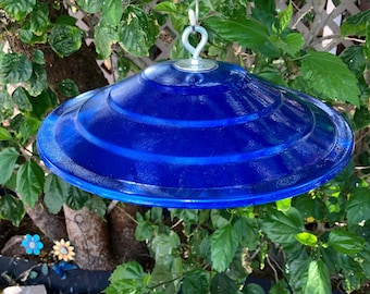 May include: A blue metal bird feeder with a rounded, tiered top and a hanging hook. The feeder is suspended from a wire.