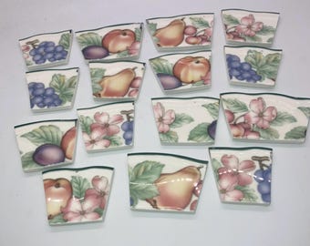 May include: A set of 15 ceramic tile pieces featuring a variety of fruit and floral designs. The tiles are white with green borders and feature images of pears, plums, grapes, apples, and flowers.