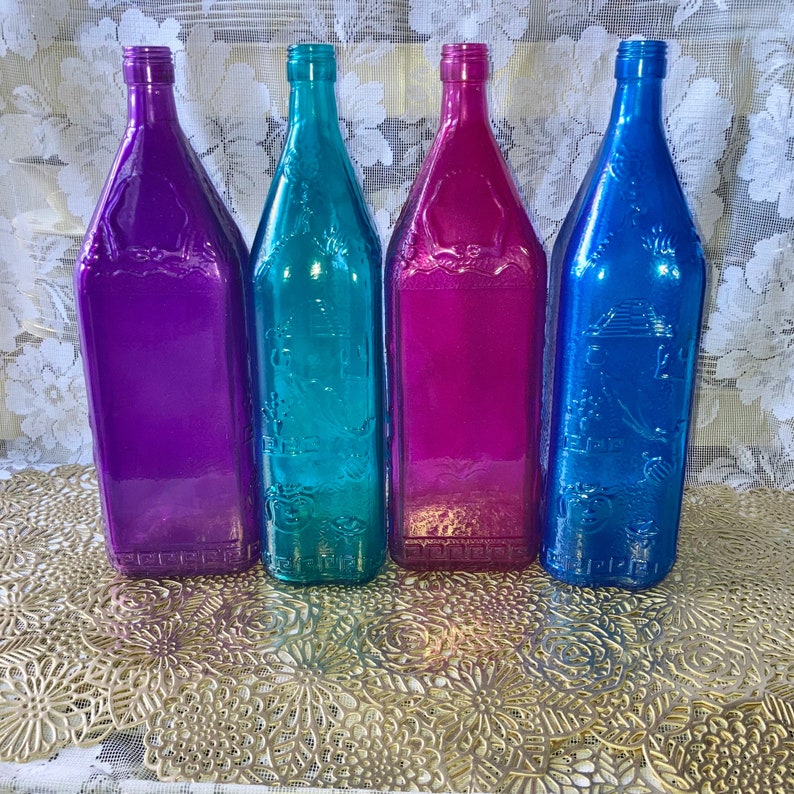 May include: Four glass bottles with a textured surface. The bottles are in shades of purple, teal, pink, and blue.
