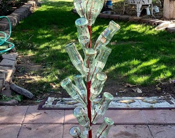 May include: A red metal bottle tree with a circular base and a central pole supporting multiple clear glass bottles. The bottles are arranged to resemble branches, creating a unique outdoor decorative piece.