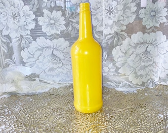 May include: A bright yellow glass bottle with a rounded bottom and a tall, slender neck. The bottle is sitting on a gold-colored, decorative surface.