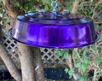 May include: A glossy, deep purple metal dome-shaped feeder with a smooth, reflective finish. The top features a central silver-colored metal eye bolt and hook assembly for hanging, secured with small clear fasteners on the circular surface.
