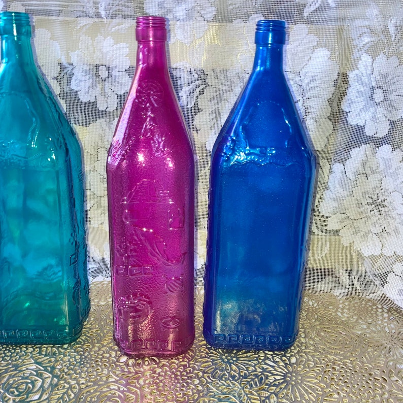 May include: Three glass bottles with a textured surface. The bottles are teal, magenta, and blue.
