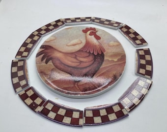 May include: A circular ceramic tile featuring a painted rooster in a landscape with clouds, surrounded by eight curved border tiles. Each border tile displays a repeating checkered pattern in dark red and cream colors, framing the central image.
