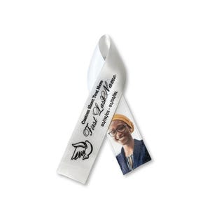 May include: A white satin ribbon folded into a awareness loop shape. The ribbon features black printed text that reads Custom Short Text Here, First LastName, and 01/01/01 - 01/01/01, a black line drawing of a dove, and a color photograph of a person.