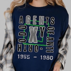 May include: A navy blue long-sleeved t-shirt with a graphic print of the text "AGENTS OF ORTH" in a black and green box with the text "1965 - 1980" below.