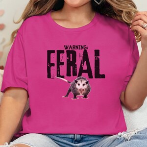 May include: A pink t-shirt with a black graphic that says "WARNING: FERAL" with a picture of a possum underneath the text.