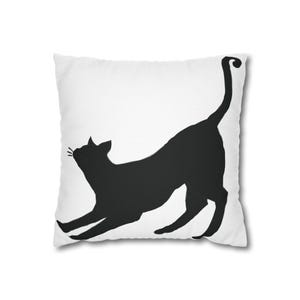 May include: White throw pillow with a black silhouette of a cat stretching. The cat is facing to the left and has its tail curled up.