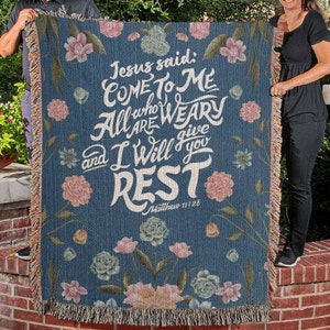 K&ouml;nnte beinhalten: Eine blaue gewebte Wolldecke mit einem Blumenmuster und dem Text "Jesus sagte: Kommt zu mir, alle, die ihr m&uuml;hselig und beladen seid, so will ich euch Ruhe geben. Matth&auml;us 11,28"