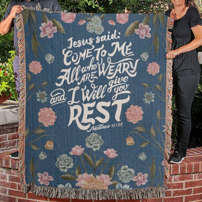 K&ouml;nnte beinhalten: Eine blaue gewebte Wolldecke mit einem Blumenmuster und dem Text "Jesus sagte: Kommt zu mir, alle, die ihr m&uuml;hselig und beladen seid, so will ich euch Ruhe geben. Matth&auml;us 11,28"