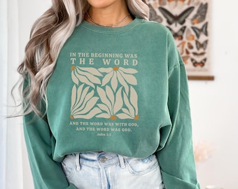 May include: A green sweatshirt with a white graphic design of stylized flowers and the text "IN THE BEGINNING WAS THE WORD AND THE WORD WAS WITH GOD, AND THE WORD WAS GOD. John 1:1"