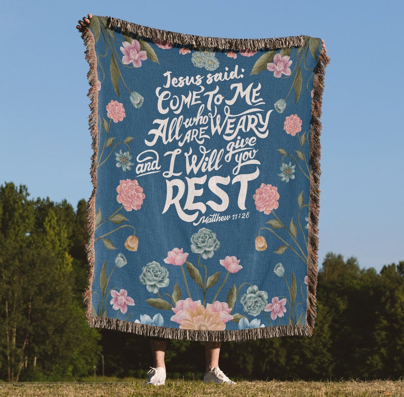 K&ouml;nnte beinhalten: Eine blaue gewebte Wolldecke mit einem Blumenmuster und dem Text "Jesus sagte: Kommt zu mir, alle, die ihr m&uuml;hselig und beladen seid, so will ich euch Ruhe geben. Matth&auml;us 11,28"