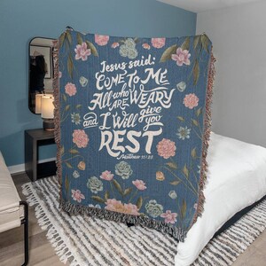 K&ouml;nnte beinhalten: Eine blaue, gewebte Wolldecke mit einem Blumenmuster und dem Text "Jesus sagte: Kommt zu mir, alle, die ihr m&uuml;hselig und beladen seid, so will ich euch Ruhe geben. Matth&auml;us 11,28"