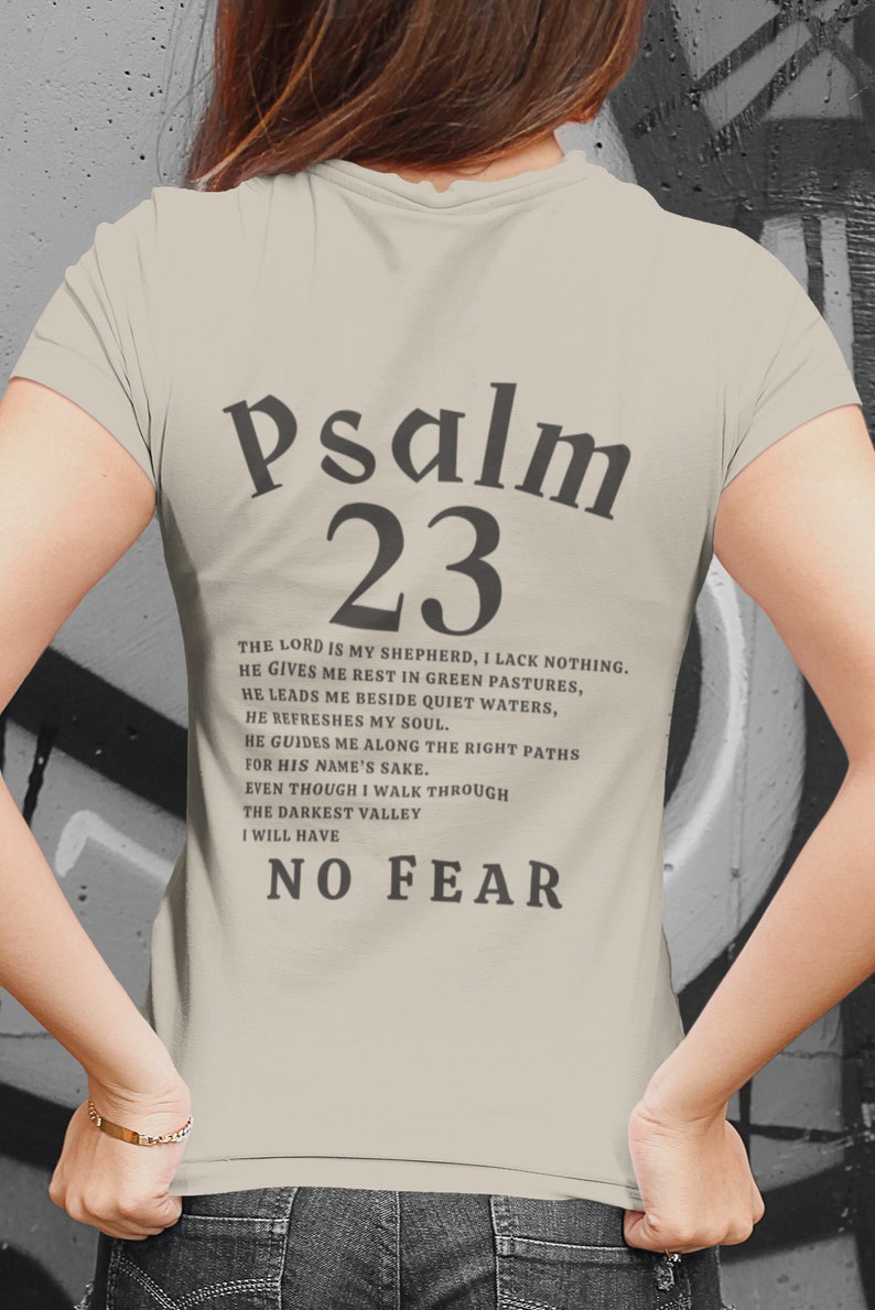 Może przedstawiać: Beżowa koszulka z napisem "Psalm 23" w kolorze czarnym. Tekst kontynuuje werset z Biblii: "Pan jest moim pasterzem, niczego mi nie braknie. Na zielonych pastwiskach daje mi odpoczynek, nad spokojne wody mnie prowadzi. Odnawia moje siły, prowadzi mnie po ścieżkach sprawiedliwości dla swego imienia. Choćbym chodził doliną cienia śmierci, nie ulęknę się zła, bo Ty jesteś ze mną; tw&oacute;j kij i twoja laska są moją pociechą."