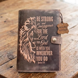 May include: A brown leather journal with a lion design and the text "BE STRONG and Courageous FOR THE Lord YOUR God IS WITH YOU WHEREVER YOU GO Joshua 1:9". Includes a "GENUINE LEATHER" tag.