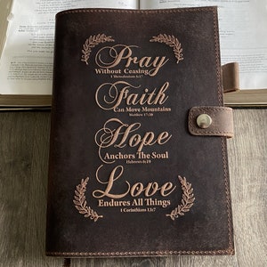 May include: Brown leather journal with gold embossed lettering. The text reads "Pray Without Ceasing", "Faith Can Move Mountains", "Hope Anchors The Soul", and "Love Endures All Things".