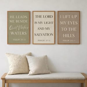 May include: Three framed wall art pieces with inspirational quotes. The frames are a light brown colour. The text is in a serif font. The first frame has the text "He Leads Me Beside Quiet Waters Waters Psalm 23:2". The second frame has the text "The Lord Is My Light And My Salvation Psalm 27:1". The third frame has the text "I Lift Up My Eyes To The Hills Psalm 121:1".