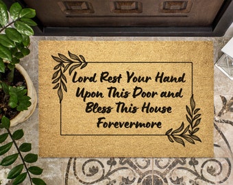 May include: A brown coir doormat with the text "Lord Rest Your Hand Upon This Door and Bless This House Forevermore" in a black frame with leafy vines on either side.